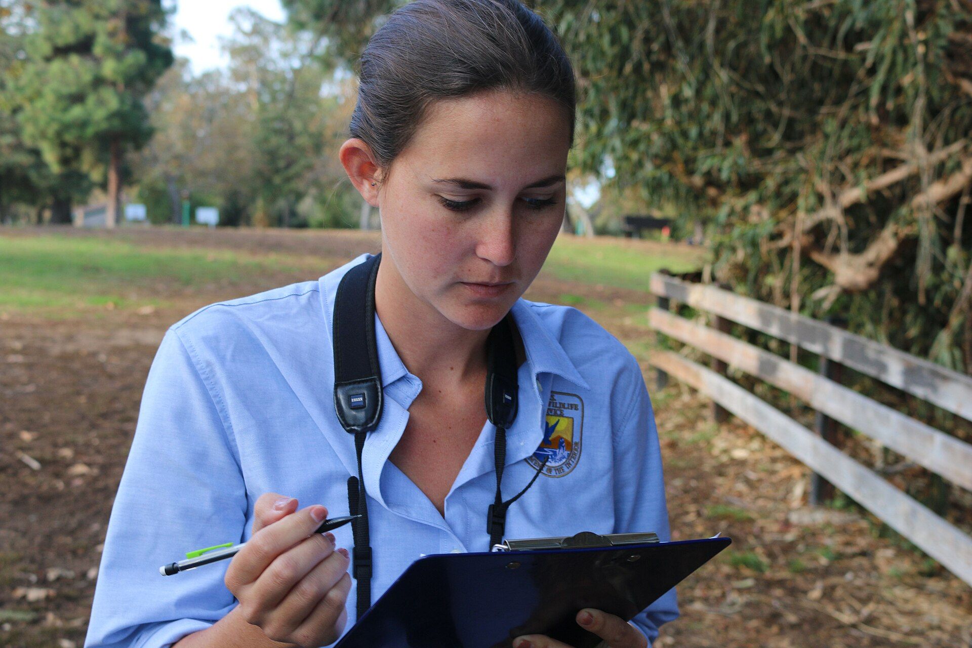 A wildlife biologist in uniform writing counts on a clipboard outdoors
