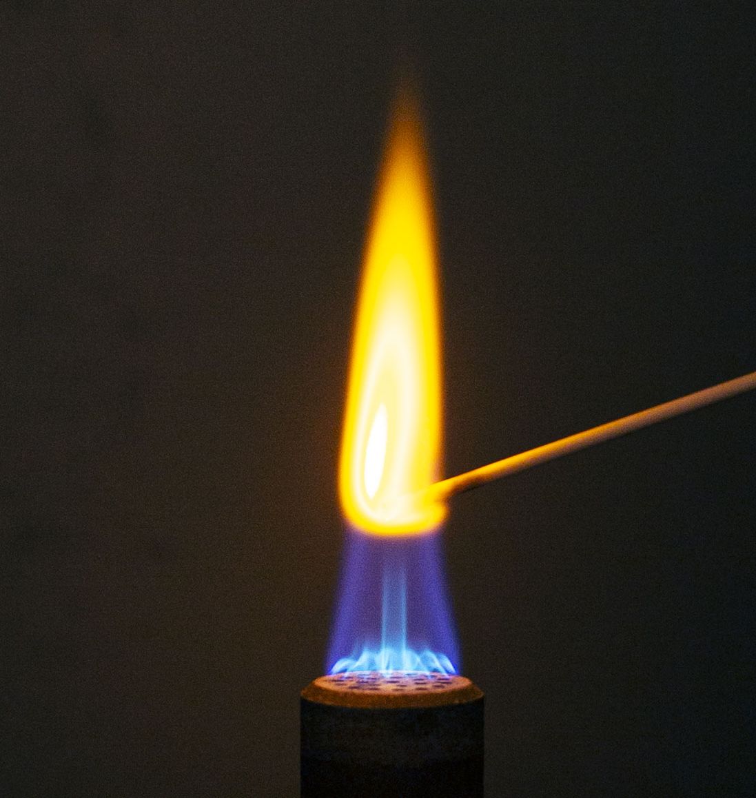 A bright yellow-orange flame on a lab burner, made by holding salt on a wooden stick in the flame