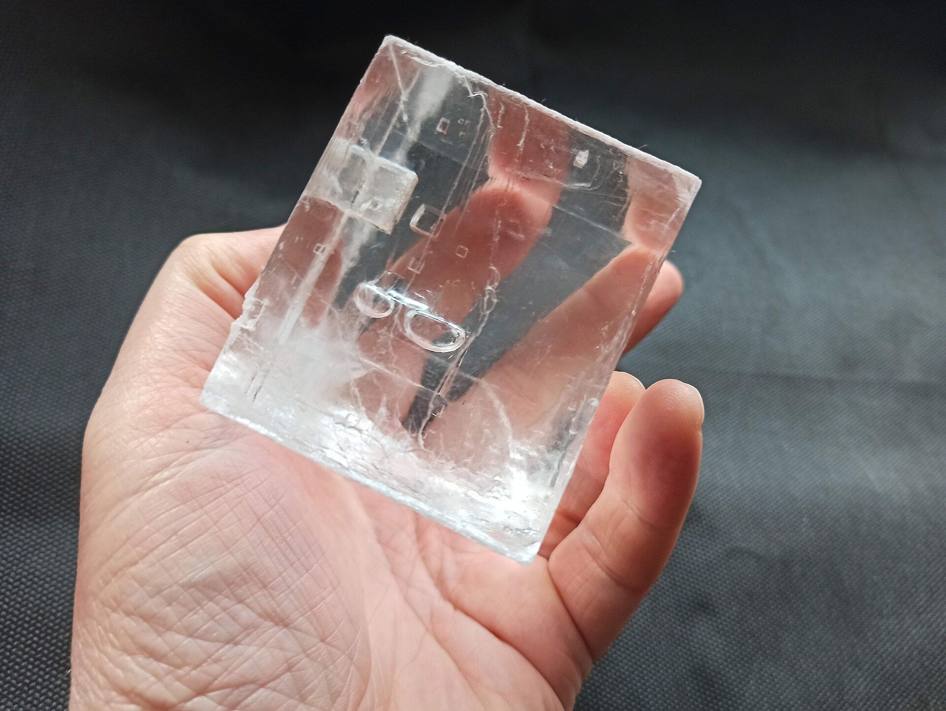 A hand holding a large, clear, cube-shaped crystal of salt