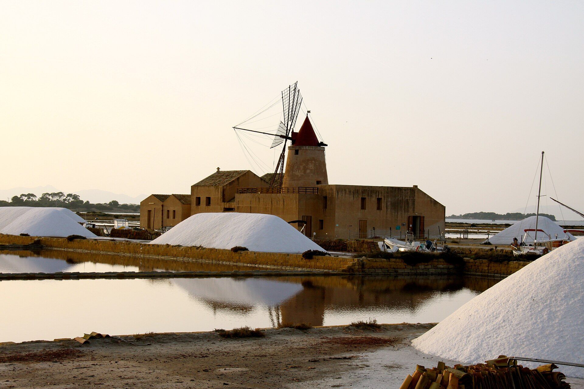 White piles of sea salt beside shallow ponds, with a windmill behind them