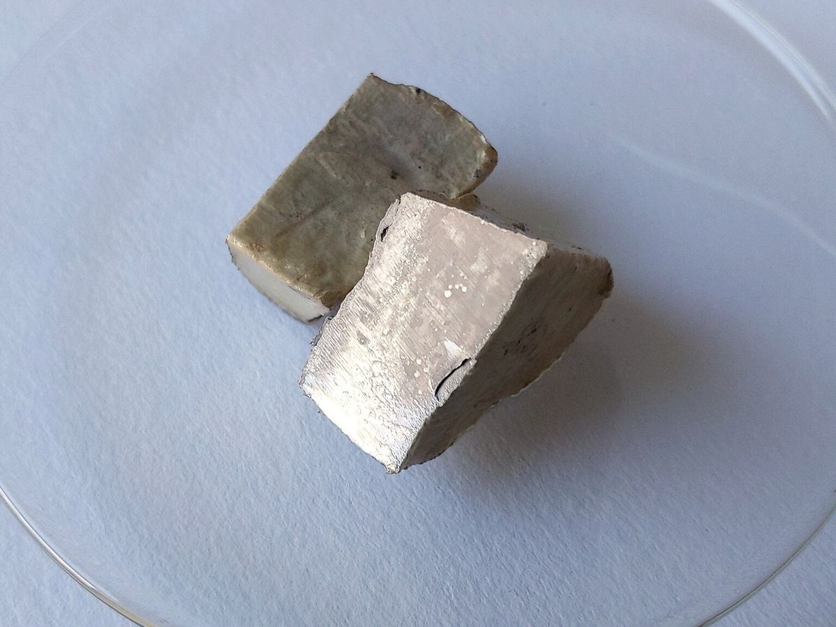 A small block of sodium metal in a glass dish, with one freshly cut shiny silver side