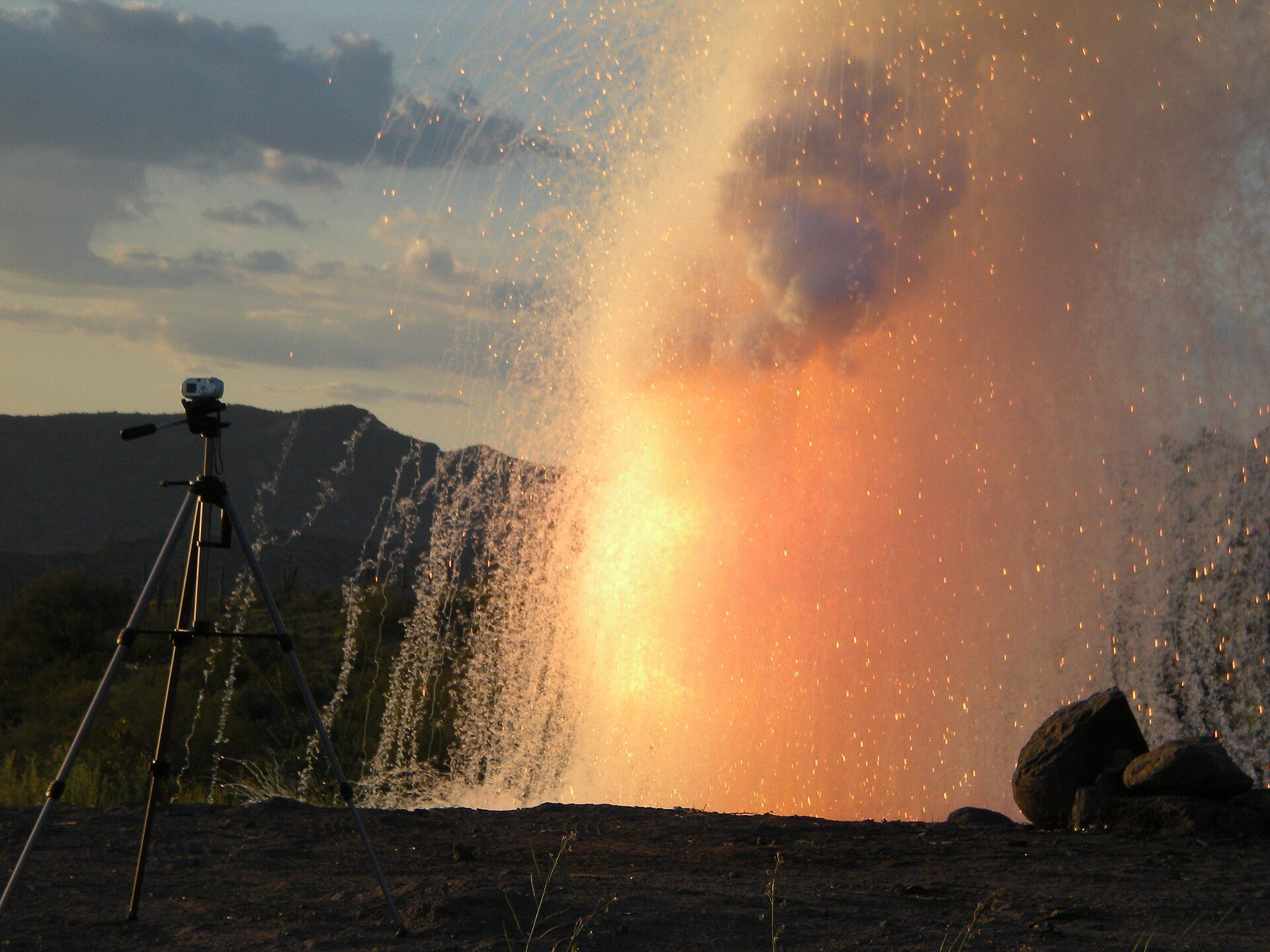 A tall orange fireball and a spray of sparks where water was poured on sodium metal outdoors
