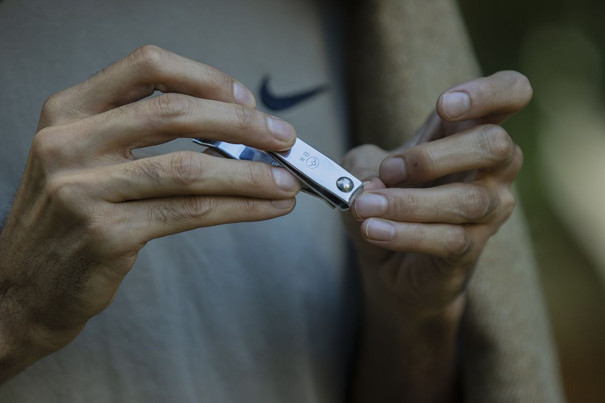 Two hands holding a metal nail clipper, with short clean fingernails in view