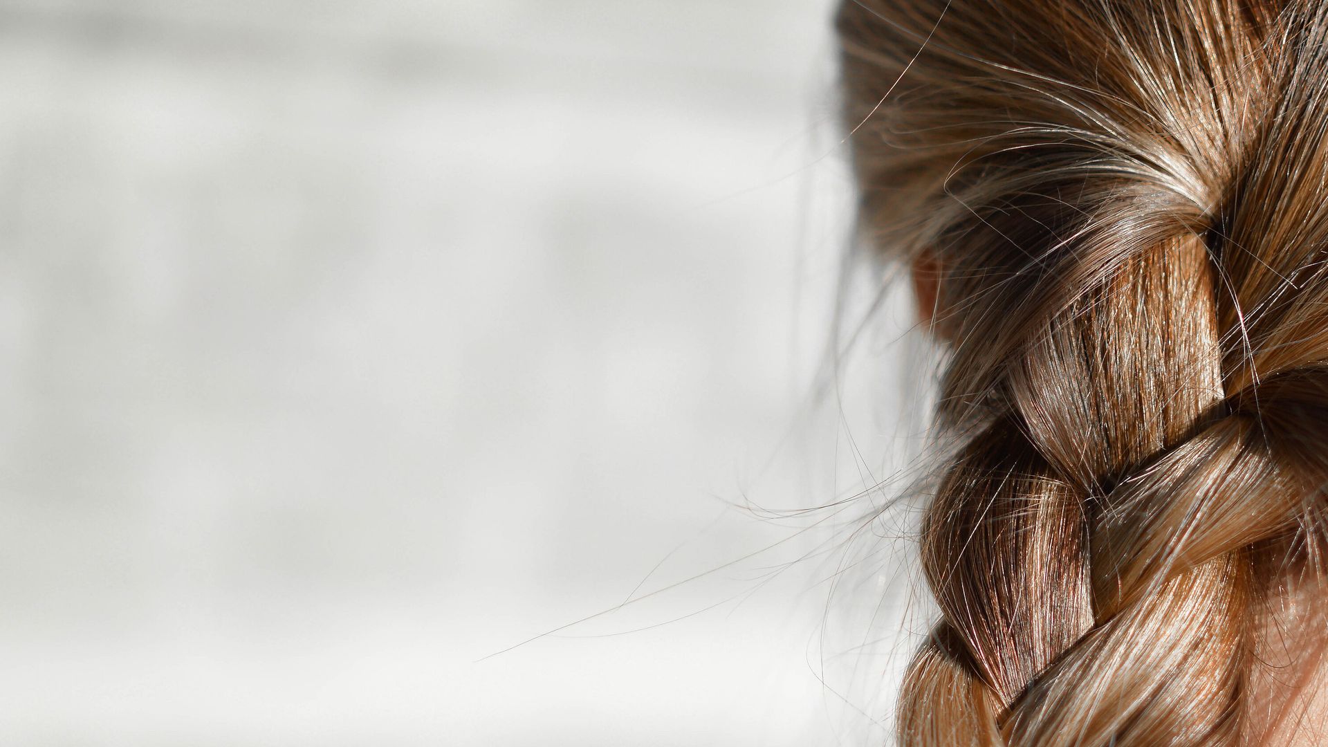 Close view of a thick braid of light brown hair, with loose strands catching the light
