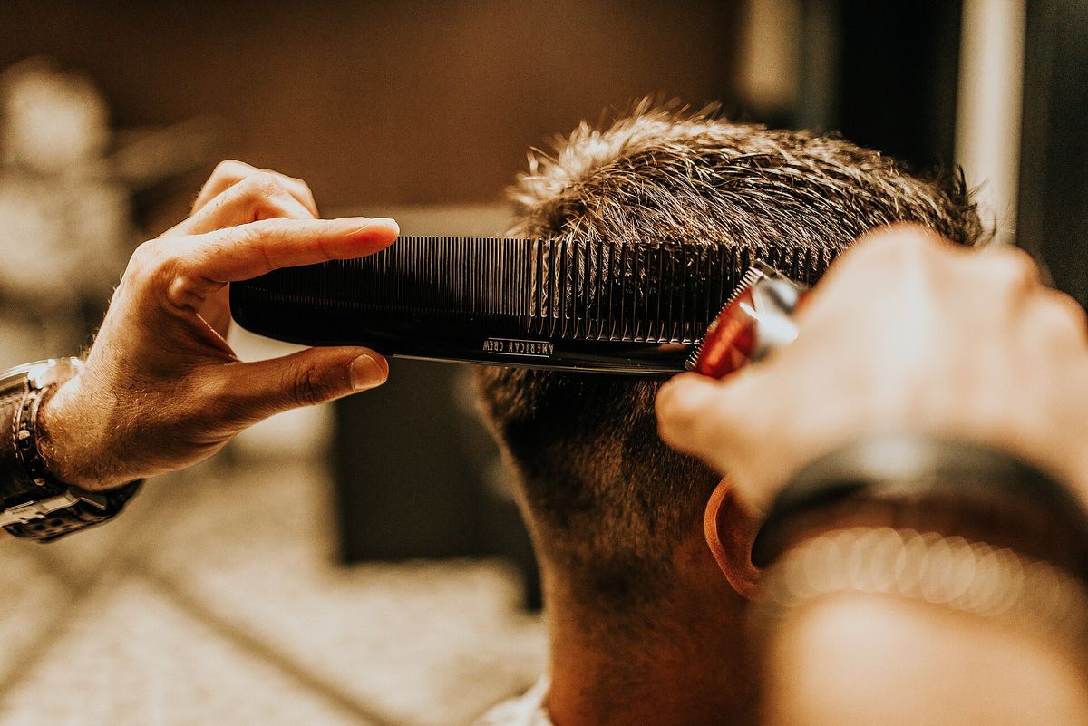 A barber holds a comb against the back of a man’s head and trims the hair with clippers