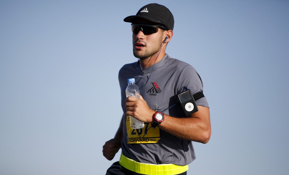 A runner in a cap and sunglasses carrying a water bottle during a marathon on a hot, clear day