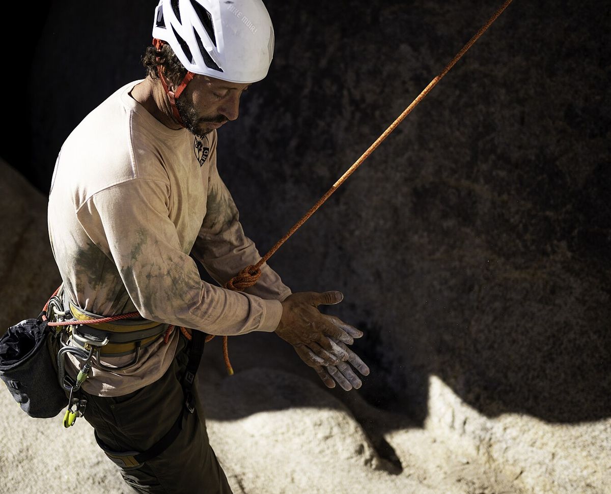 A rock climber in a helmet rubbing white chalk onto his hands beside a boulder