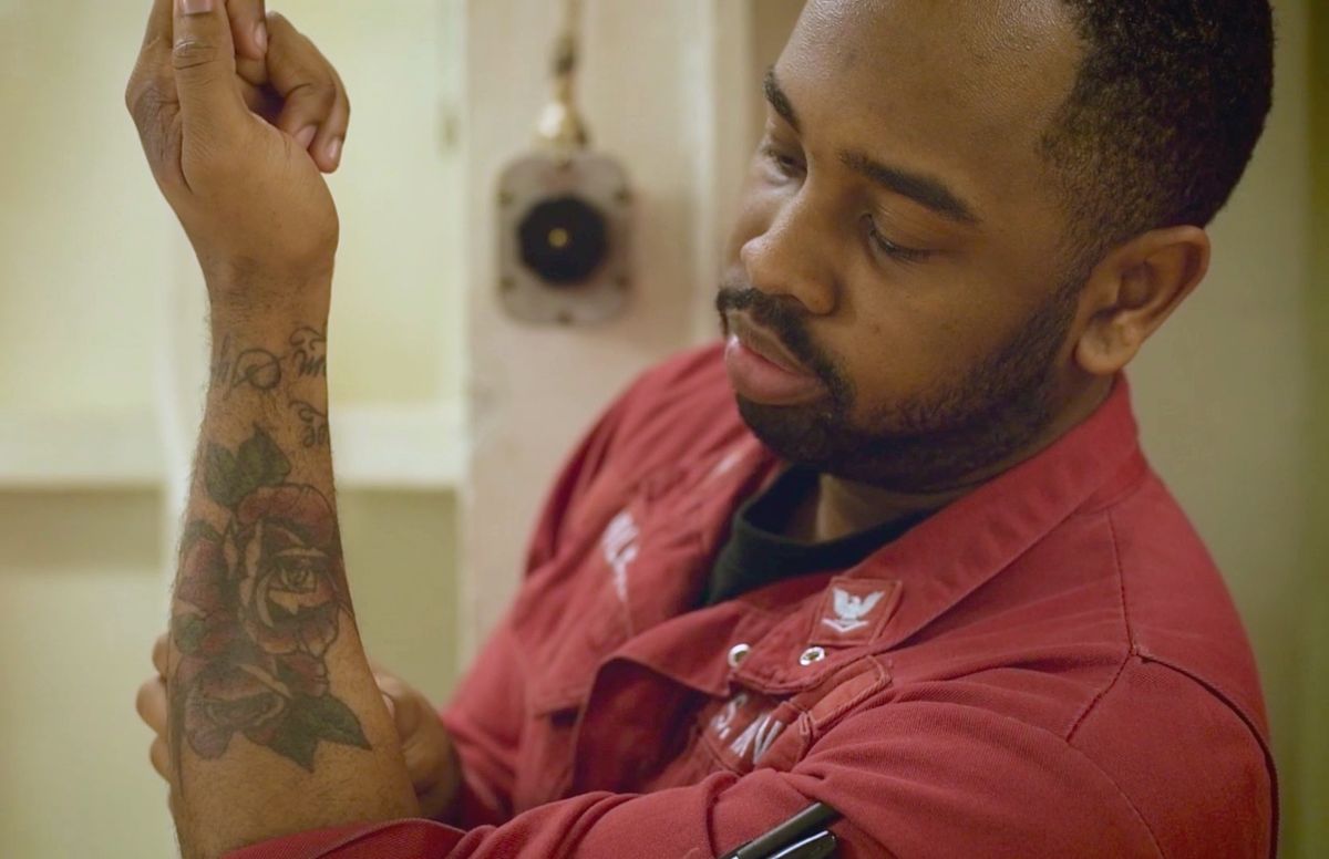 A sailor holding up his forearm to show a rose tattoo