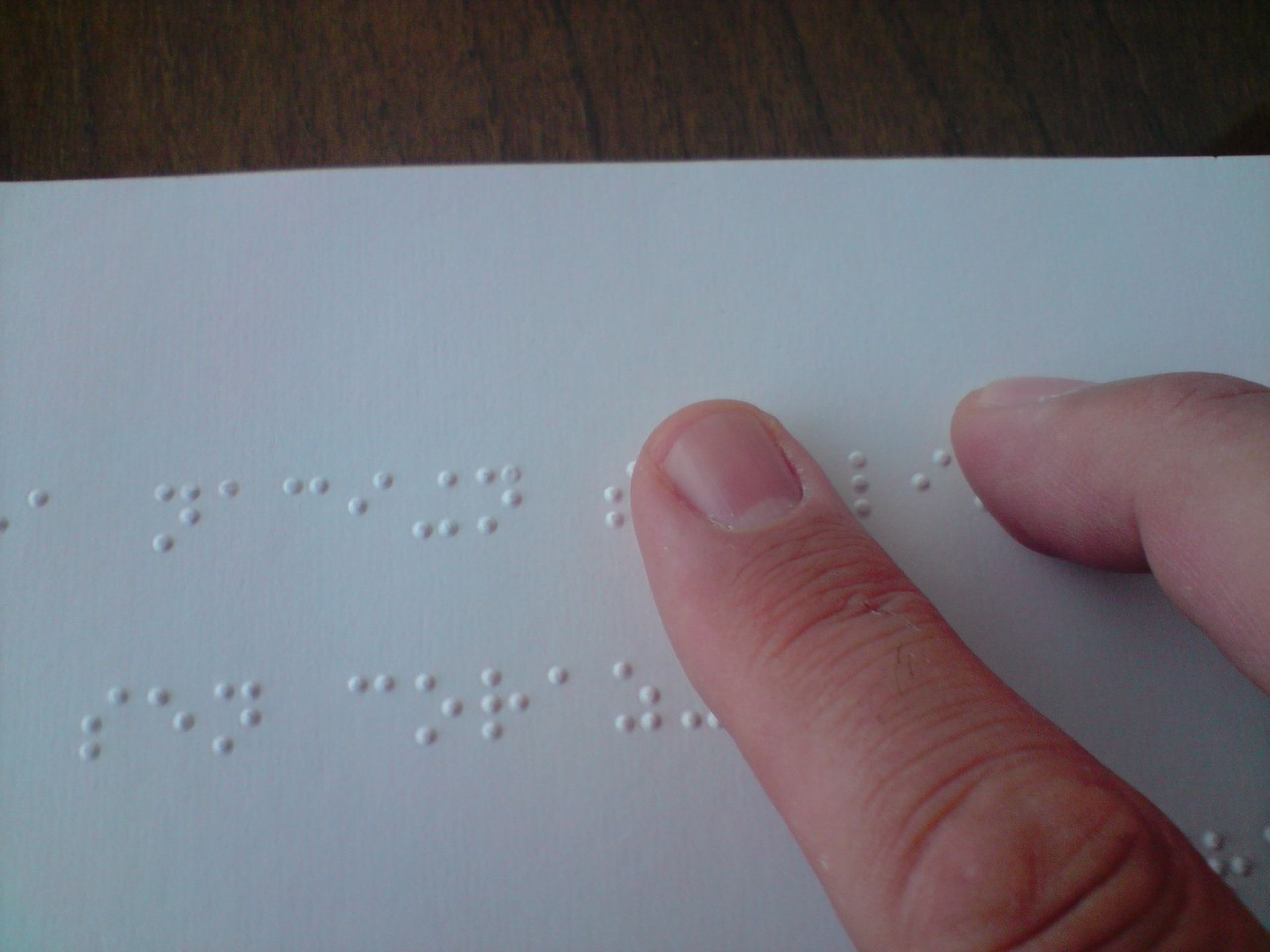 A fingertip resting on a white page of raised Braille dots