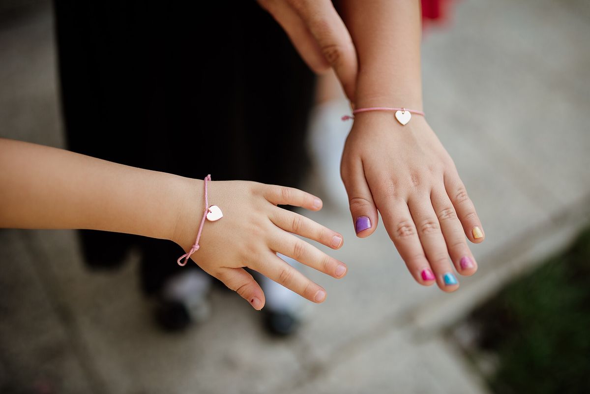 Two children’s arms and hands, one wearing a bracelet, with painted fingernails