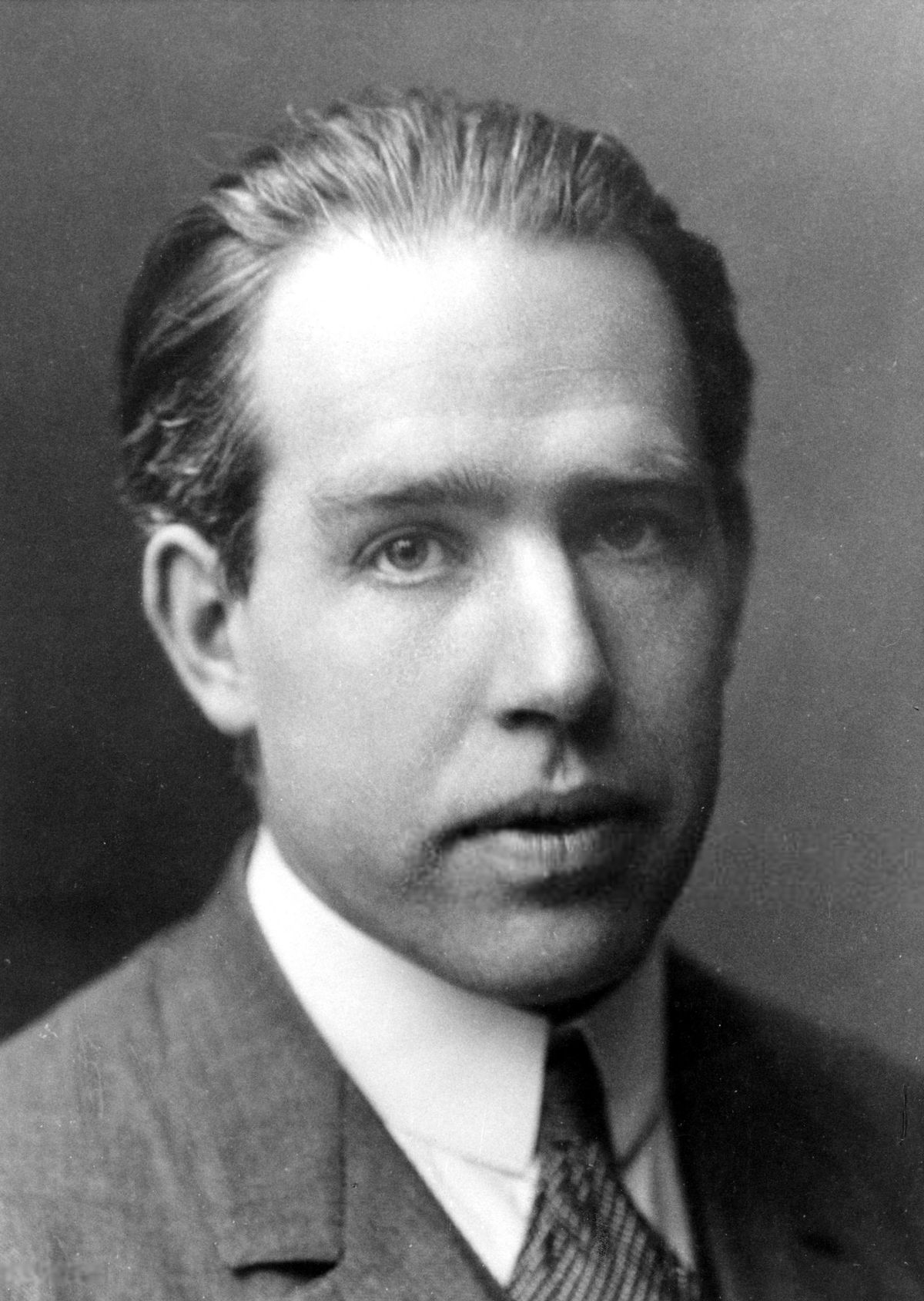 A black and white portrait of Niels Bohr as a young man in a suit and tie