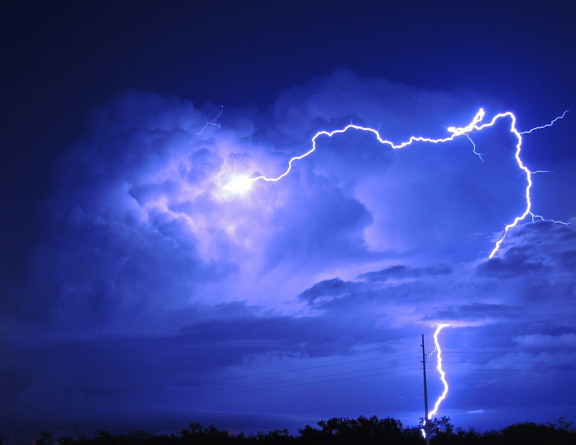A bright bolt of lightning crossing a deep blue storm cloud at night and striking the ground