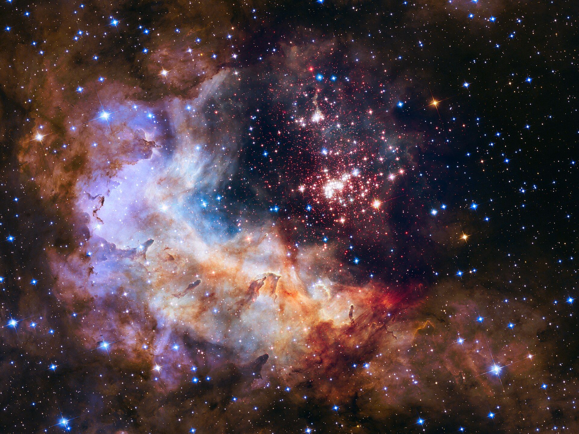 A cluster of bright young stars inside glowing red and blue clouds of gas, photographed by the Hubble Space Telescope